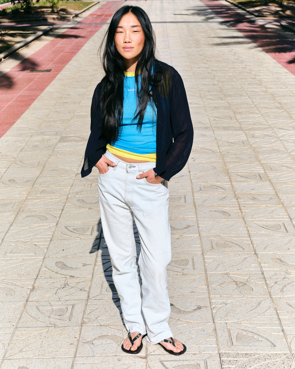 Person wearing a blue top, black cardigan, white pants and black barefoot sandals on a paved walkway.