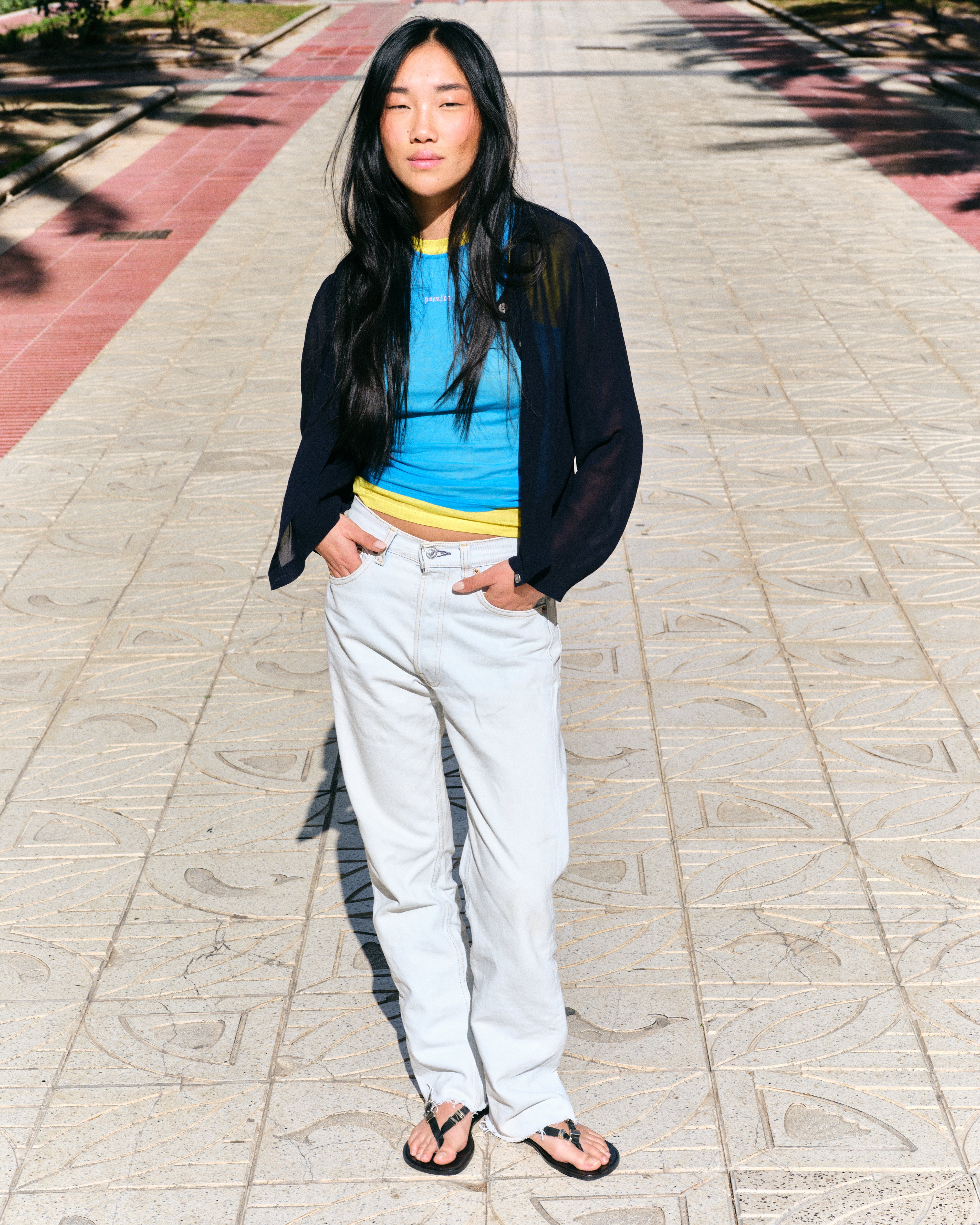 Person wearing a blue top, black cardigan, white pants and black barefoot sandals on a paved walkway.