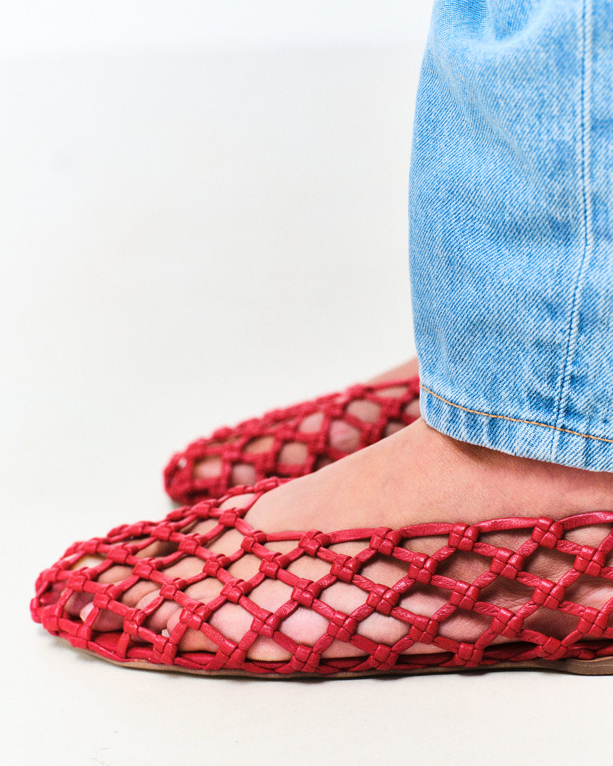 Red woven flats worn with blue jeans on a white background