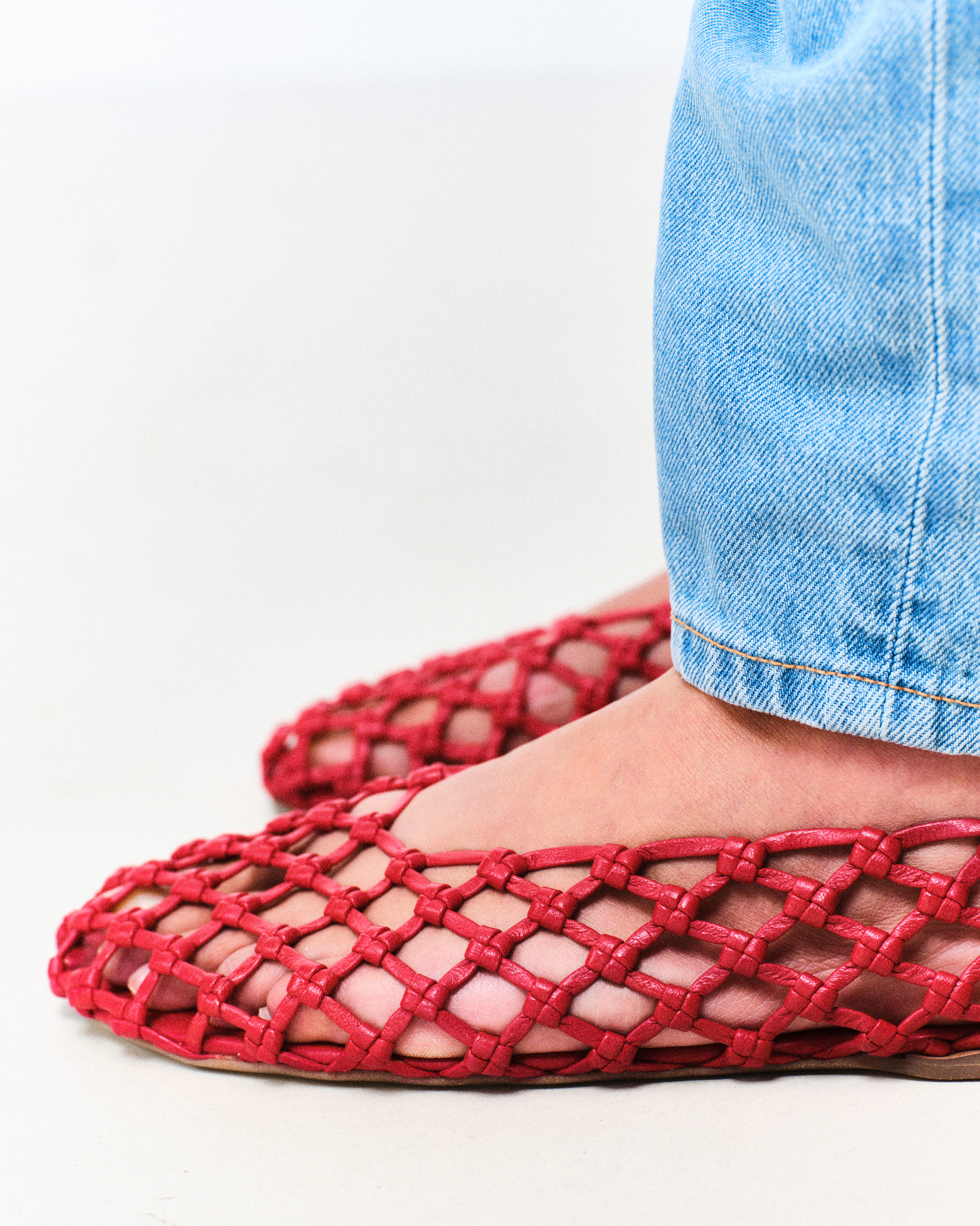 Red woven flats worn with blue jeans on a white background
